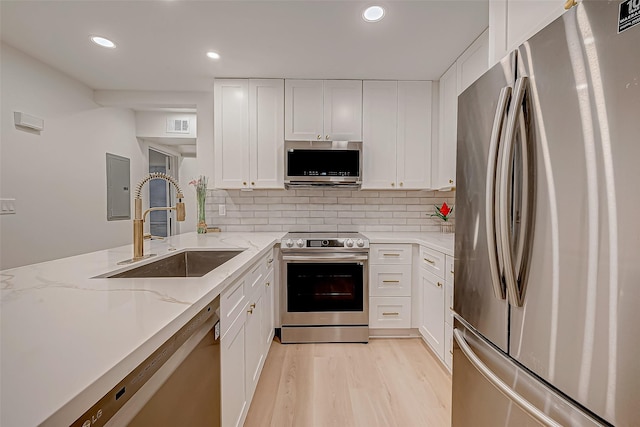 kitchen with light stone counters, stainless steel appliances, sink, white cabinets, and light hardwood / wood-style floors