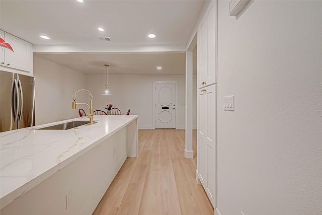 kitchen with sink, decorative light fixtures, light stone counters, white cabinetry, and stainless steel refrigerator