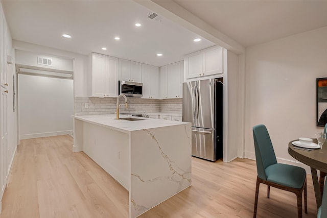 kitchen featuring light stone countertops, light wood-type flooring, stainless steel appliances, sink, and white cabinets