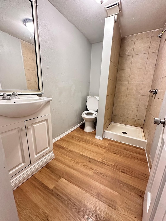 bathroom featuring hardwood / wood-style floors, vanity, toilet, a textured ceiling, and a tile shower