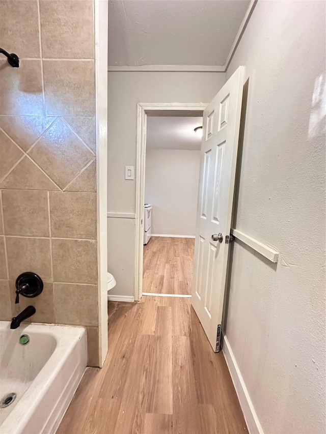 bathroom with hardwood / wood-style flooring, tiled shower / bath combo, toilet, and crown molding