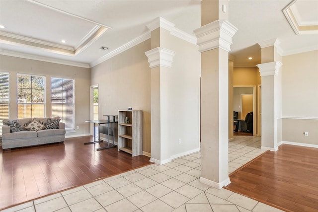 unfurnished living room with light tile patterned floors, ornate columns, a raised ceiling, and crown molding