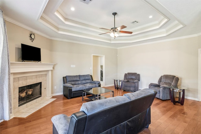 living room with a tray ceiling, a tile fireplace, and crown molding