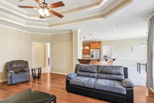 living room featuring a raised ceiling, crown molding, ceiling fan, and light hardwood / wood-style floors