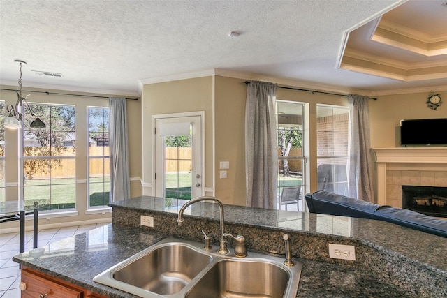 kitchen featuring sink, hanging light fixtures, a textured ceiling, a tiled fireplace, and ornamental molding