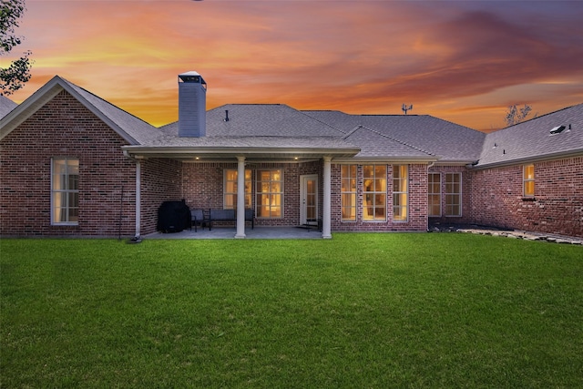 back house at dusk featuring a yard and a patio