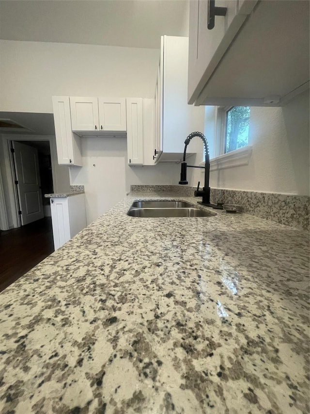 kitchen with white cabinetry, sink, and light stone countertops