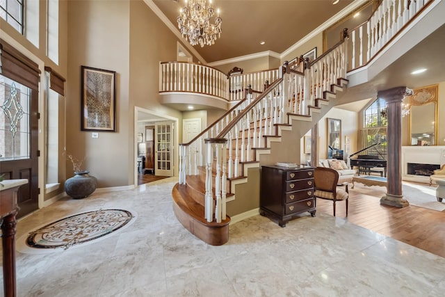 foyer entrance with decorative columns, crown molding, a towering ceiling, and a chandelier