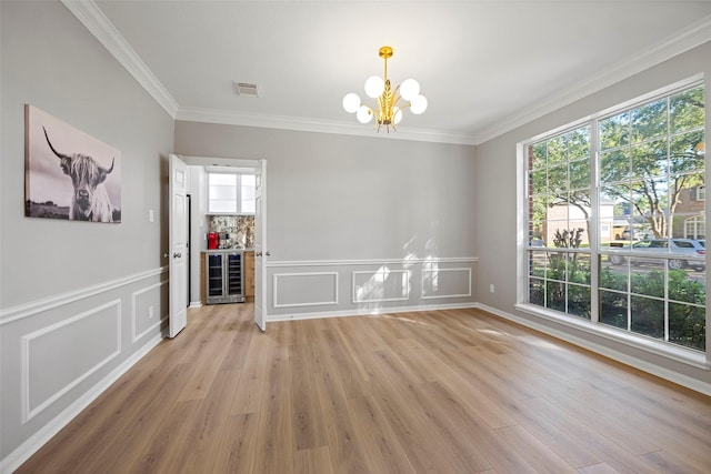 unfurnished dining area with ornamental molding, beverage cooler, light wood-type flooring, and an inviting chandelier