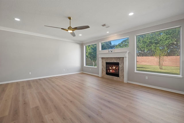 unfurnished living room with a tiled fireplace, ceiling fan, crown molding, and light hardwood / wood-style floors