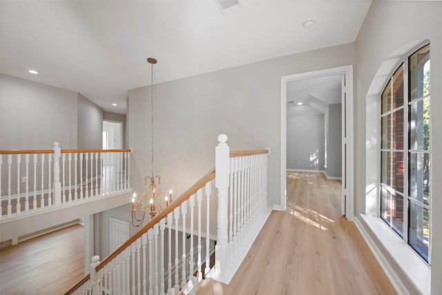 hallway with an inviting chandelier and light wood-type flooring