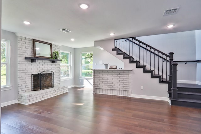 unfurnished living room featuring a brick fireplace and dark wood-type flooring