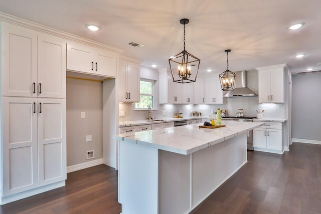 kitchen with pendant lighting, wall chimney range hood, sink, a kitchen island, and white cabinetry