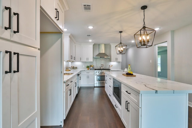 kitchen featuring wall chimney exhaust hood, stainless steel appliances, a kitchen island, decorative light fixtures, and white cabinets