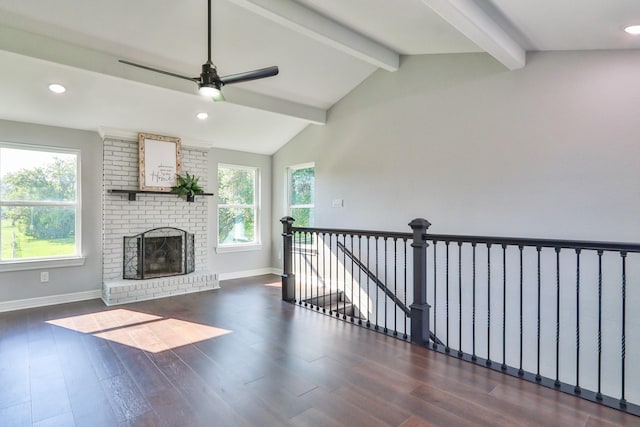 unfurnished living room featuring lofted ceiling with beams, a healthy amount of sunlight, dark wood-type flooring, and a brick fireplace