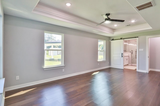 unfurnished bedroom featuring connected bathroom, ceiling fan, a raised ceiling, a barn door, and multiple windows