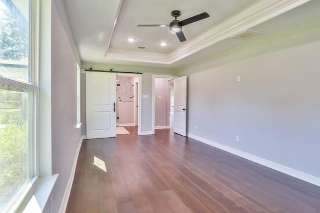 unfurnished bedroom featuring ceiling fan, a barn door, ornamental molding, a tray ceiling, and dark hardwood / wood-style flooring