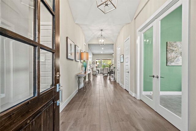 corridor with french doors, vaulted ceiling, light hardwood / wood-style flooring, and a notable chandelier