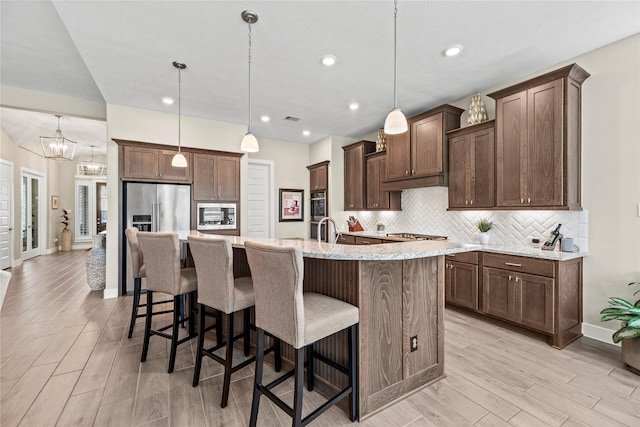 kitchen with backsplash, a breakfast bar, hanging light fixtures, and a kitchen island with sink