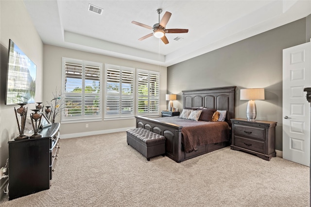 carpeted bedroom with a raised ceiling and ceiling fan