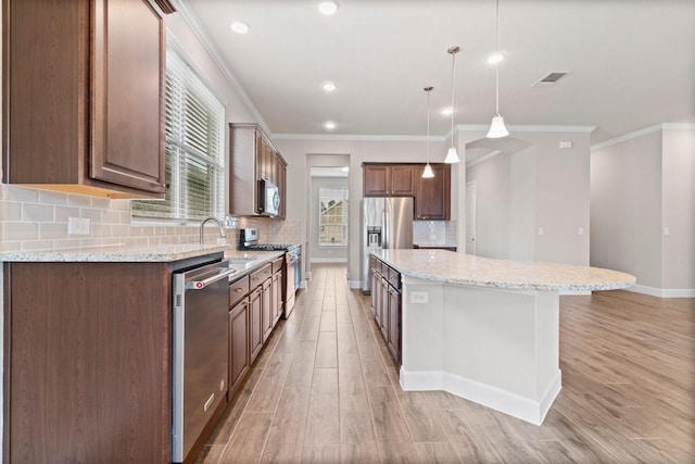 kitchen featuring light stone countertops, appliances with stainless steel finishes, sink, pendant lighting, and a kitchen island