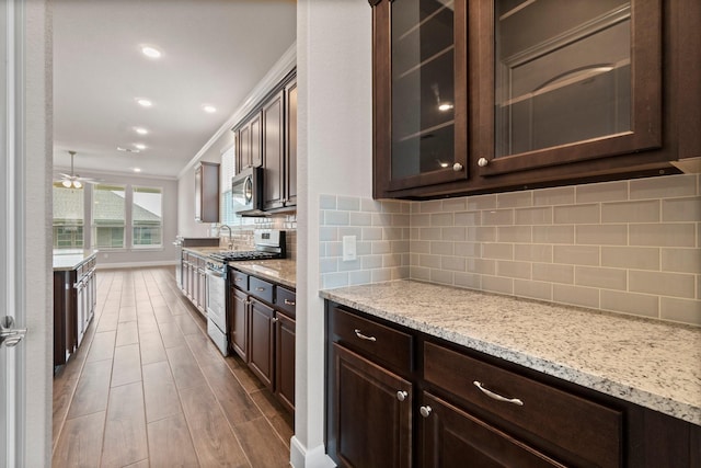 kitchen with dark brown cabinetry, light stone countertops, stainless steel appliances, tasteful backsplash, and ornamental molding