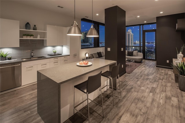 kitchen featuring white cabinetry, sink, a wall of windows, stainless steel dishwasher, and a breakfast bar