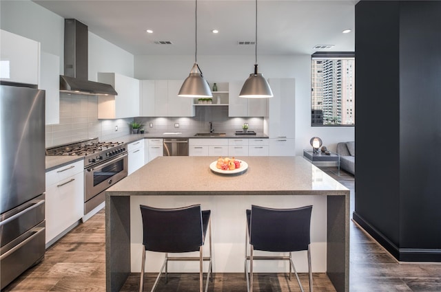 kitchen featuring white cabinetry, wall chimney exhaust hood, hanging light fixtures, a kitchen island, and appliances with stainless steel finishes