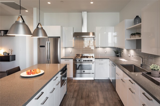 kitchen with sink, stainless steel appliances, wall chimney range hood, dark stone counters, and white cabinets