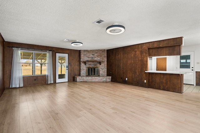 unfurnished living room with light wood-type flooring, a textured ceiling, a fireplace, and wooden walls