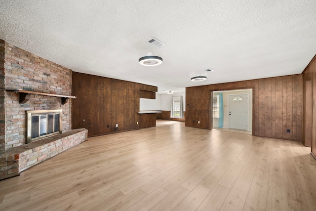 unfurnished living room featuring a textured ceiling, light hardwood / wood-style floors, a fireplace, and wooden walls