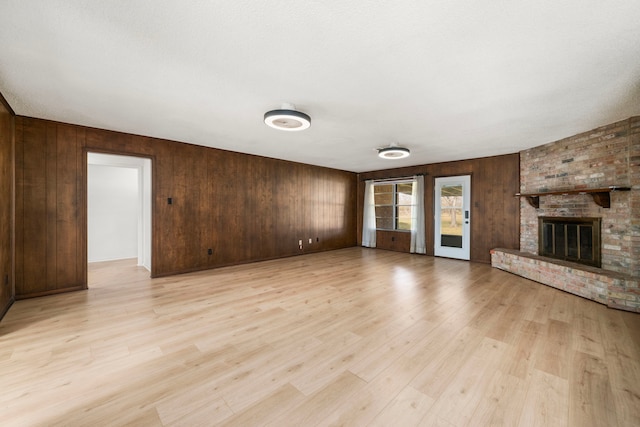 unfurnished living room featuring a brick fireplace, light hardwood / wood-style flooring, and wood walls