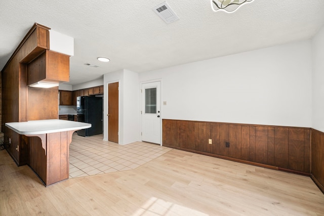 kitchen featuring light hardwood / wood-style floors, black fridge, kitchen peninsula, a textured ceiling, and a breakfast bar area