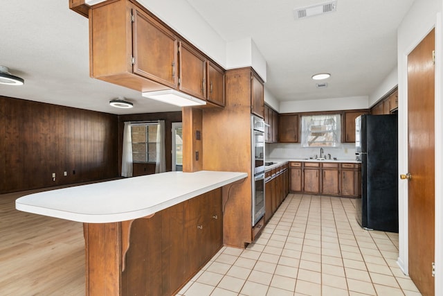 kitchen with kitchen peninsula, a kitchen bar, sink, stainless steel oven, and black refrigerator