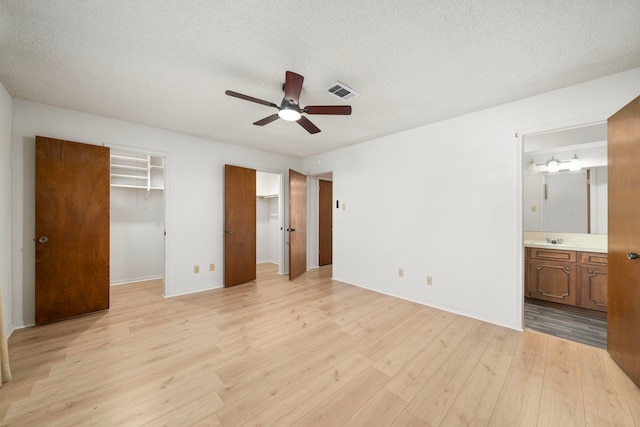 unfurnished bedroom with ceiling fan, light wood-type flooring, connected bathroom, and a textured ceiling