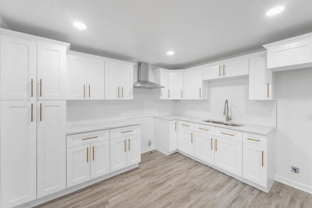 kitchen with sink, wall chimney exhaust hood, light stone counters, light hardwood / wood-style floors, and white cabinets