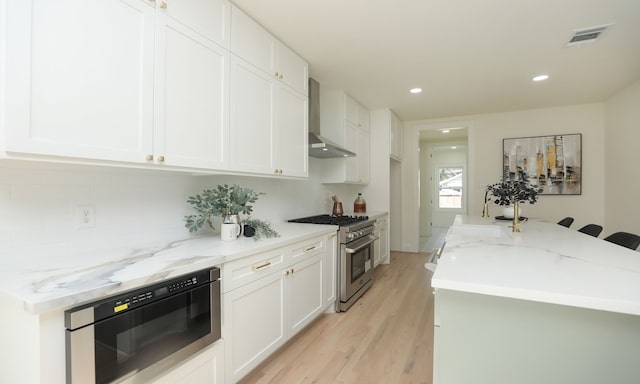 kitchen featuring high end range, light stone counters, sink, wall chimney range hood, and white cabinets