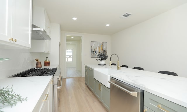 kitchen with light wood-type flooring, stainless steel dishwasher, white range with gas cooktop, sink, and white cabinets