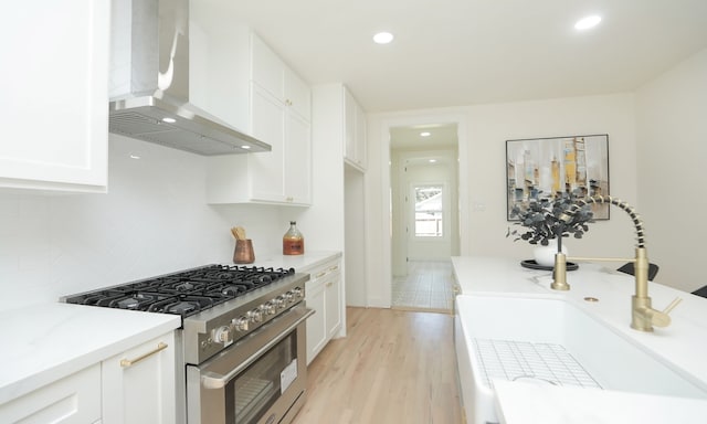 kitchen with white cabinetry, high end stainless steel range, wall chimney exhaust hood, and sink