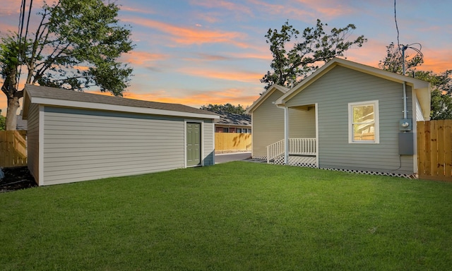 back house at dusk featuring a yard and an outbuilding