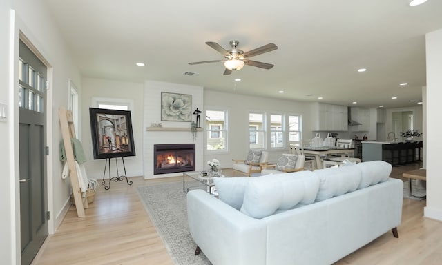 living room featuring ceiling fan, a fireplace, and light hardwood / wood-style flooring