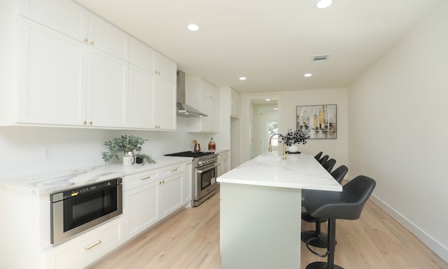 kitchen with a kitchen bar, wall chimney exhaust hood, high end stove, a center island with sink, and white cabinetry