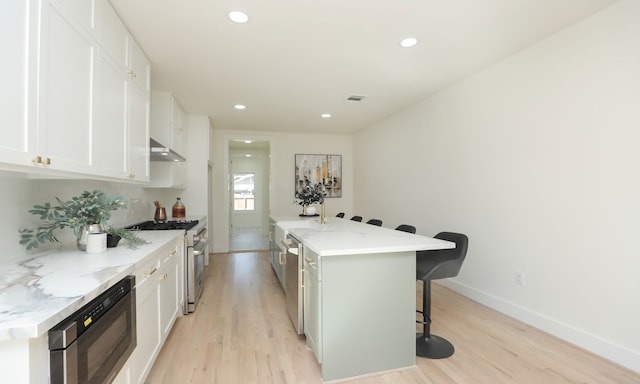 kitchen featuring white cabinetry, stainless steel appliances, light stone counters, a breakfast bar, and a center island with sink