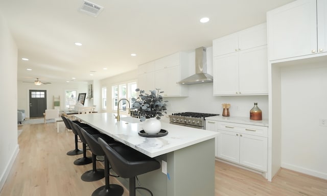 kitchen with ceiling fan, wall chimney exhaust hood, high end stainless steel range oven, a kitchen island with sink, and white cabinets