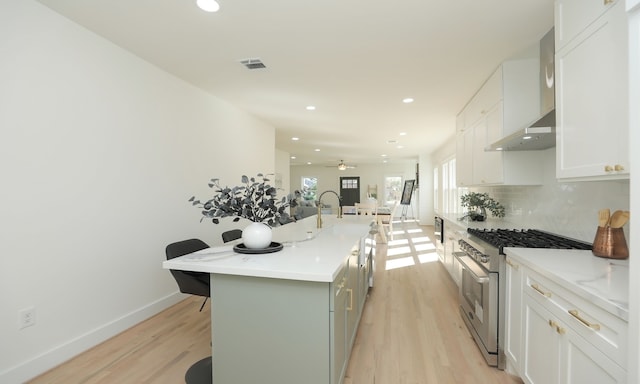 kitchen featuring white cabinets, ceiling fan, an island with sink, stainless steel range, and a kitchen bar