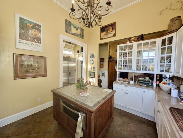 kitchen with tile counters, a kitchen island, built in refrigerator, pendant lighting, and white cabinets