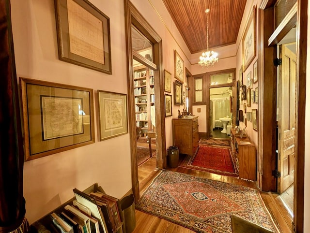 corridor with hardwood / wood-style floors, an inviting chandelier, and wooden ceiling