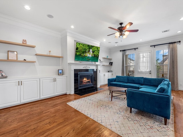 living room with ceiling fan, light wood-type flooring, a fireplace, and ornamental molding