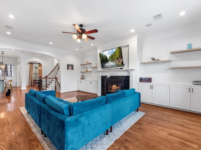 living room featuring a tile fireplace, ceiling fan, light hardwood / wood-style flooring, and ornamental molding