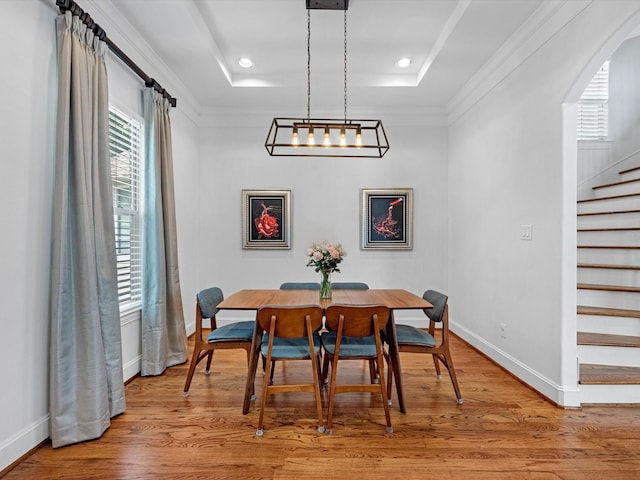 dining area featuring wood-type flooring, ornamental molding, and a tray ceiling